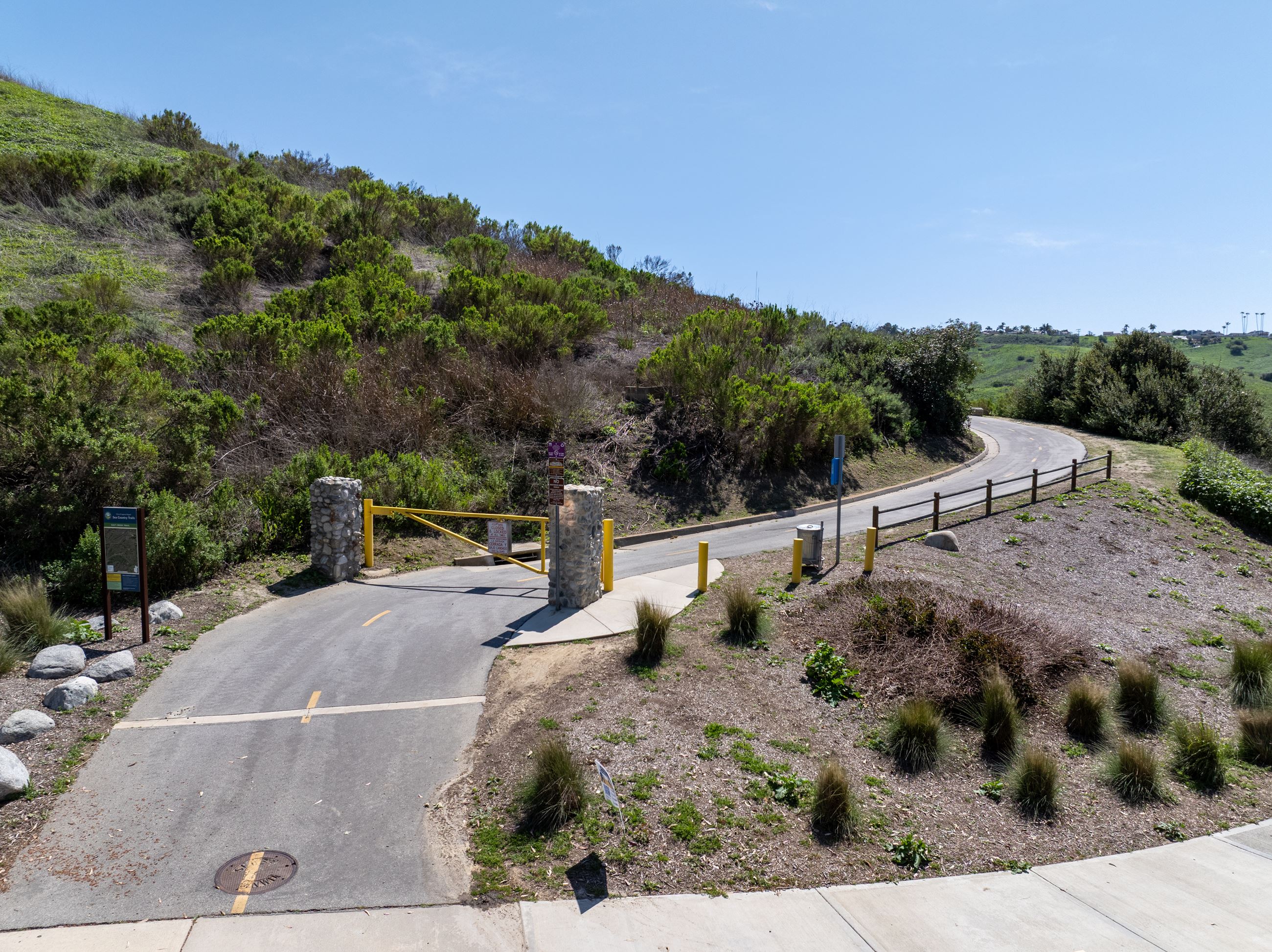 Paved multiuse trail entrance with yellow gate and hillside landscape in Laguna Niguel.