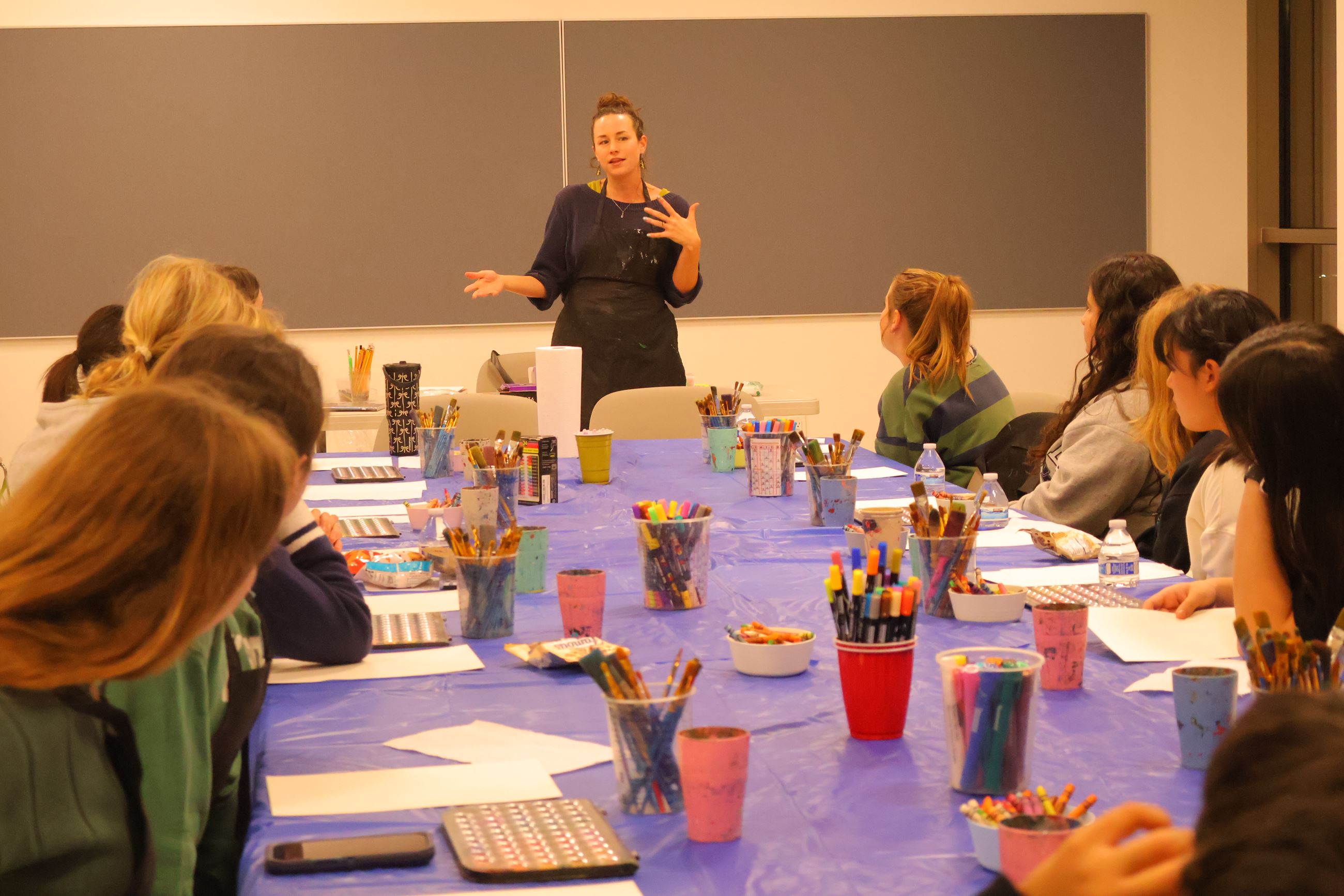 Art instructor leads a small group workshop with teens seated around a table using art supplies